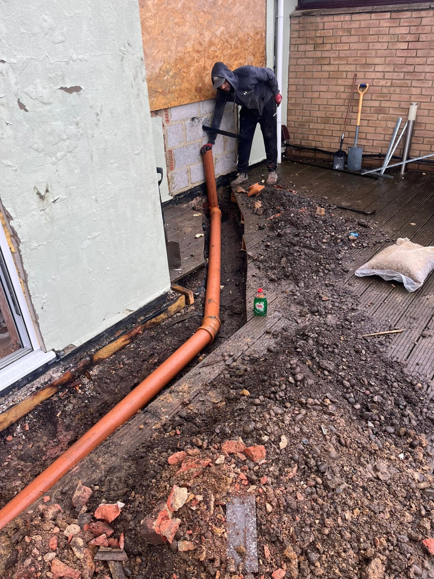External drainage installation with orange underground pipework being fitted alongside a property
