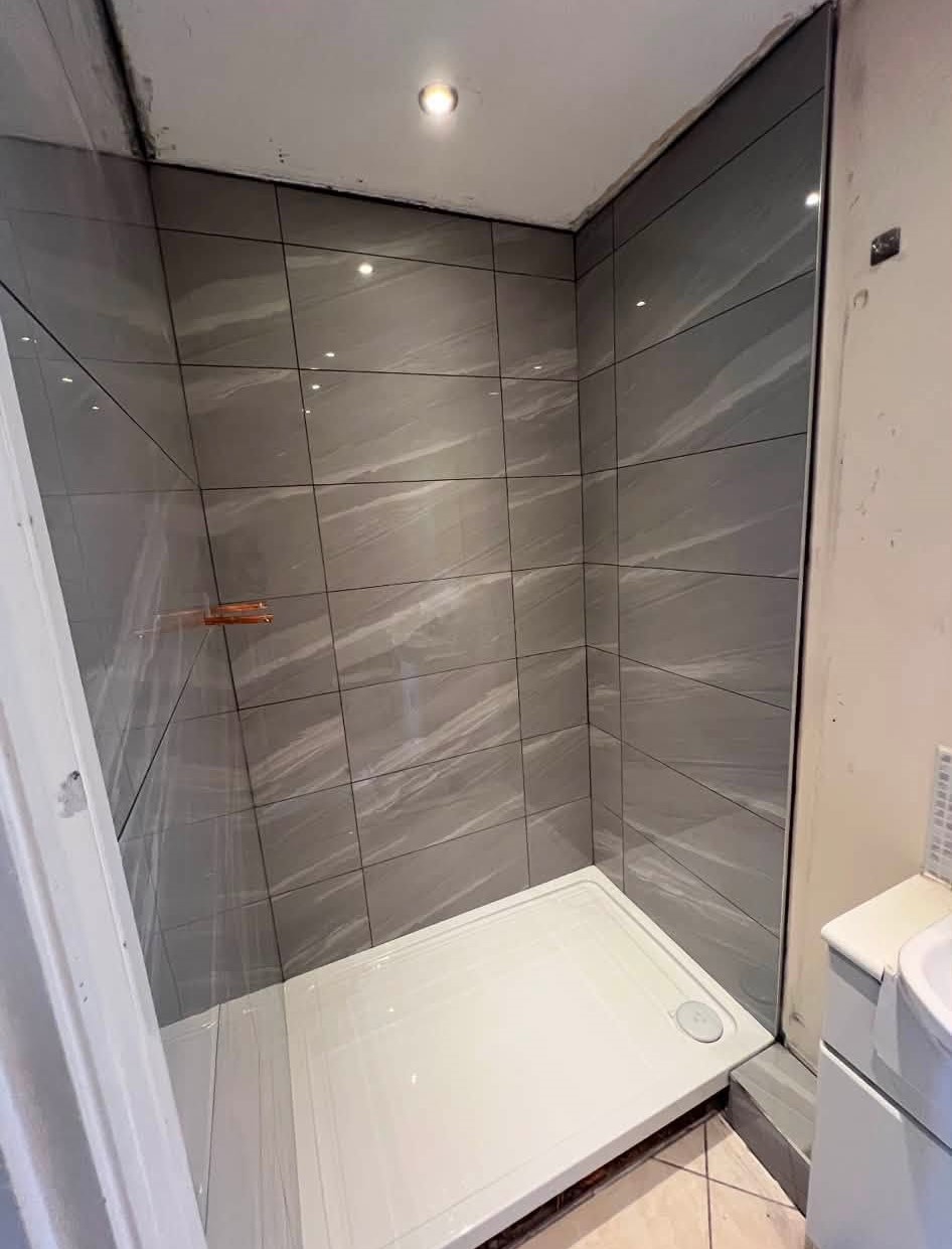 Newly tiled shower enclosure with a white tray and grey marble-effect wall tiles